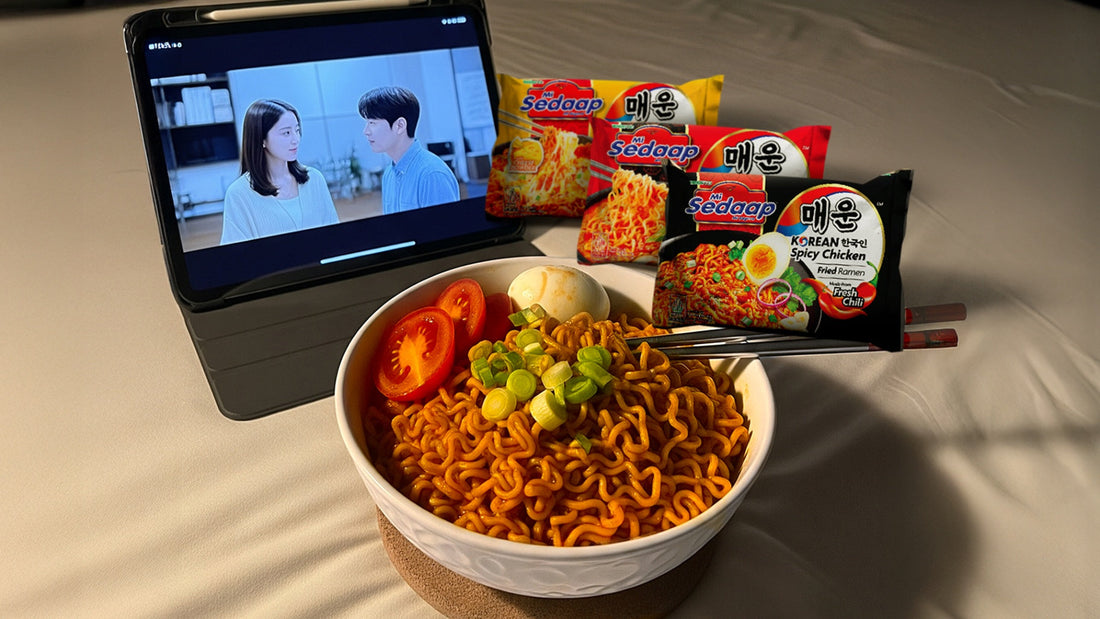 Mi Sedaap Korean Spicy Chicken ramen served with tomato, egg, and green onions, with a K-drama playing on a tablet.