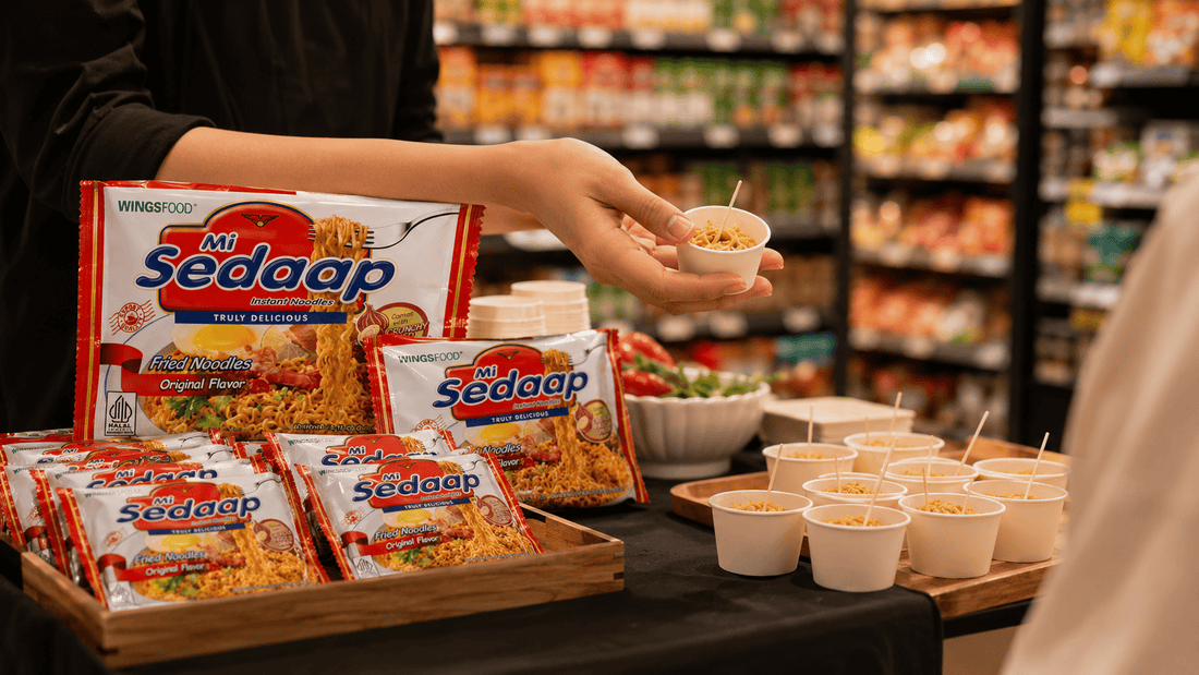 In-store demo table with Mi Sedaap Original Fried Noodles packets and small sample cups of noodles for shoppers.