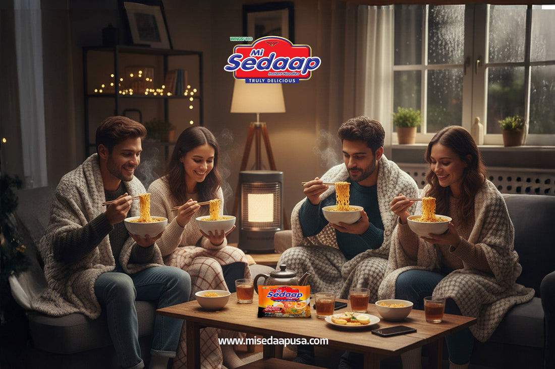 Four friends wrapped in blankets enjoying bowls of Mi Sedaap noodles together indoors on a cozy rainy evening with warm lighting and tea on the table.