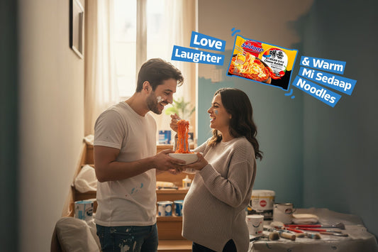 Couple laughing and sharing Mi Sedaap spicy noodles while painting their home.