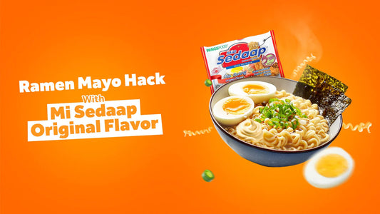 A steaming bowl of instant noodle soup topped with boiled eggs and nori on a bright orange background next to a packet of Mi Sedaap and a "Ramen Mayo Hack With Mi Sedaap Original Flavor" text graphic.