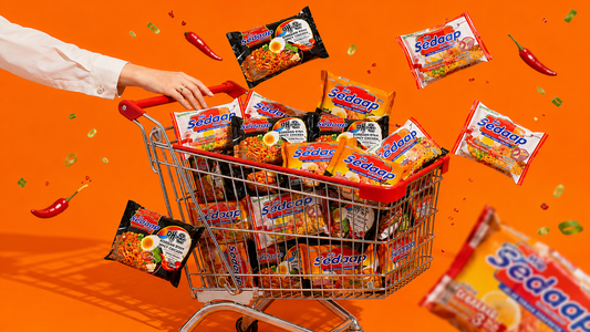 A hand pushing a shopping cart overflowing with Mi Sedaap noodle packets against a bright orange background, with extra packets and chilies falling through the air.